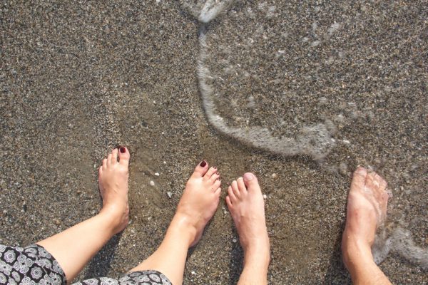 Vier Füße stehen am Strand halb im Wasser