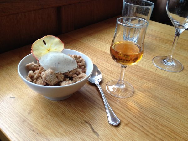 Ein Glas Calvados mit einer Dessertschuessel auf einem hözernen Tisch