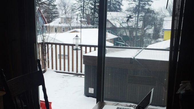 Ein dunkler Raum mit Tisch und aufgeklapptem Laptop und Schneetreiben hinter dem Fenster