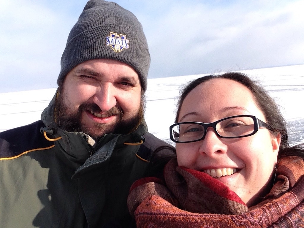 Selfie von einem Mann mit Mütze und einer Frau mit rotem Schal im Hintergrund Schnee