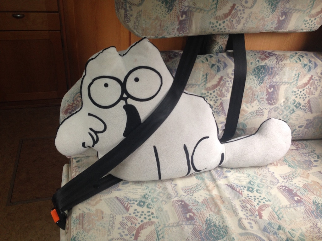 Ein Kissen in Form von Simon's Cat ist angeschnallt auf einer Bank in einem Wohnmobil