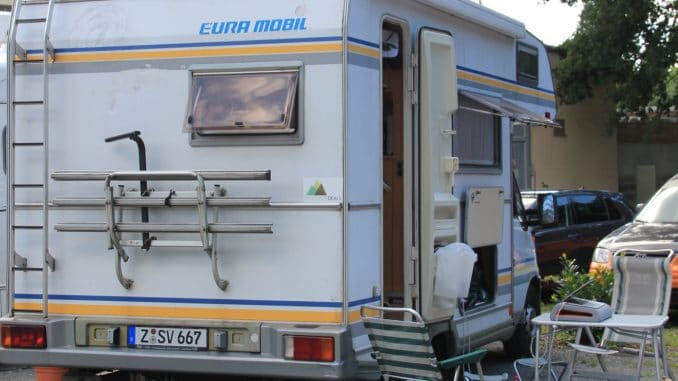 Ein Wohnmobil von eura mobil von hinten auf einem Stellplatz daneben Tisch und Stühle mit einem Laptop