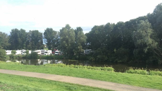 camper-camping Blick vom Deich auf einen Stellplatz mit Wohnmobilen unter Bäumen