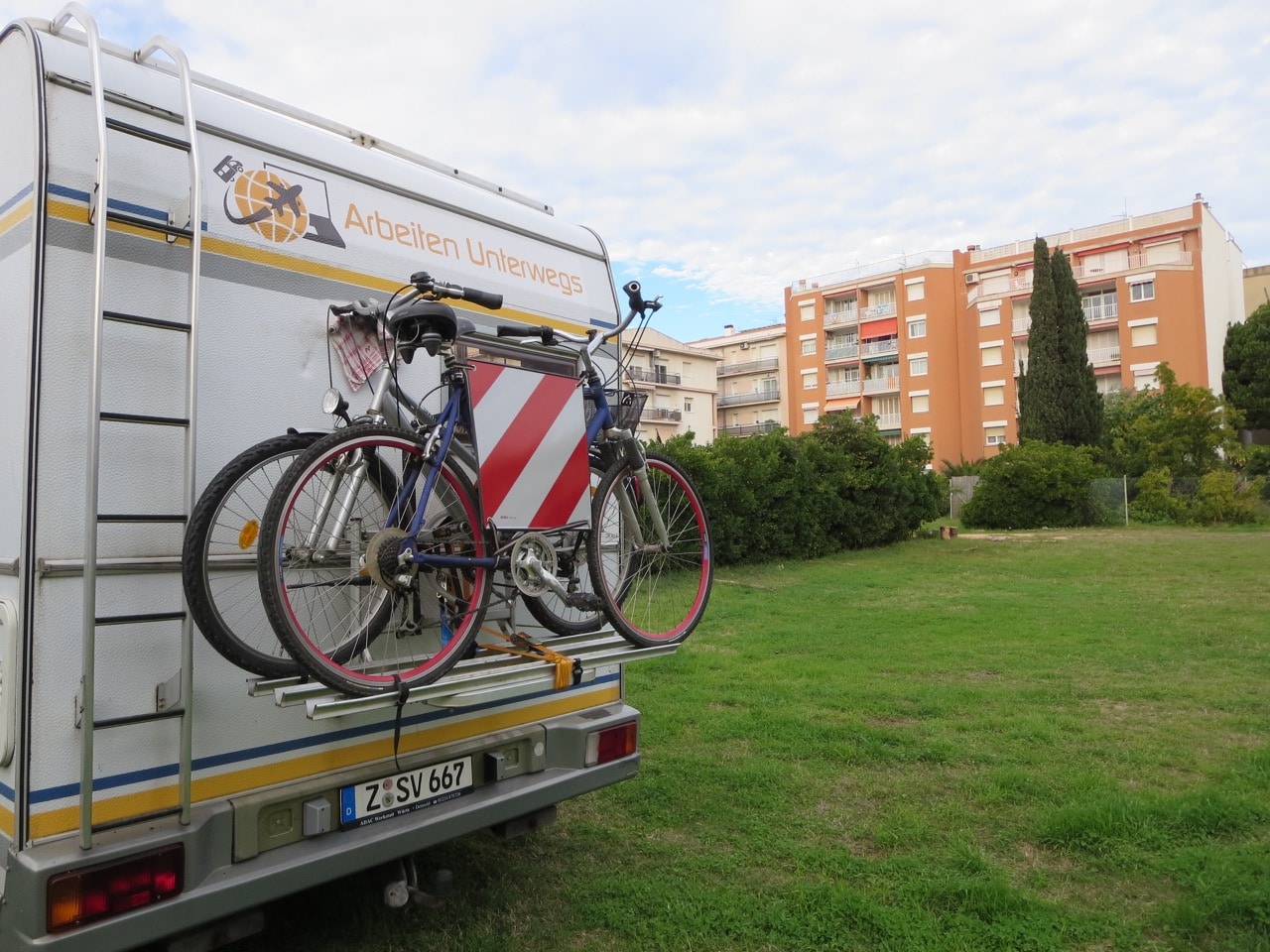 Wohnmobil mit Fahrrädern auf einer Wiese im Hintergrund Wohnblocks