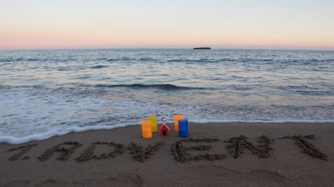frohen-ersten-advent Im Hintergrund das Meer, im Vordergrund 4 Kerzen und in den Sand geschrieben "1. Advent"