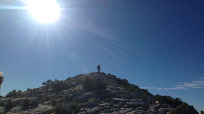 Ein Berggipfel mit einem Mann auf der Spitze mit Sonne