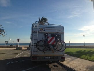 Ein Wohnmobil auf einem Parkplatz und vor dem Wohnmobil das Meer
