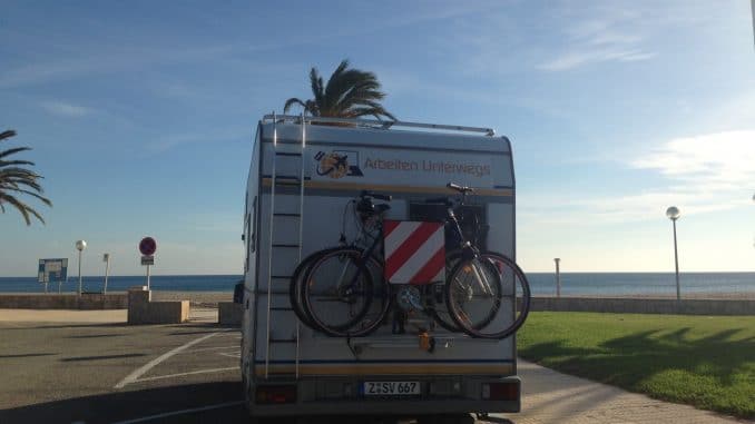 Ein Wohnmobil auf einem Parkplatz und vor dem Wohnmobil das Meer