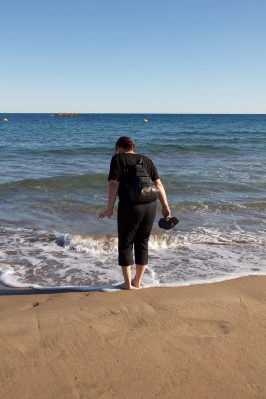 Eine Frau steht zögerlich mit den Füßen im Meer