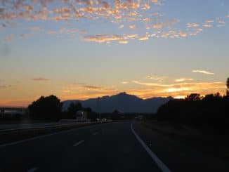 Sonne geht hinter Bergen auf einer Autobahn unter