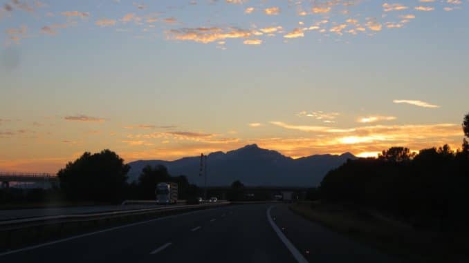 Sonne geht hinter Bergen auf einer Autobahn unter