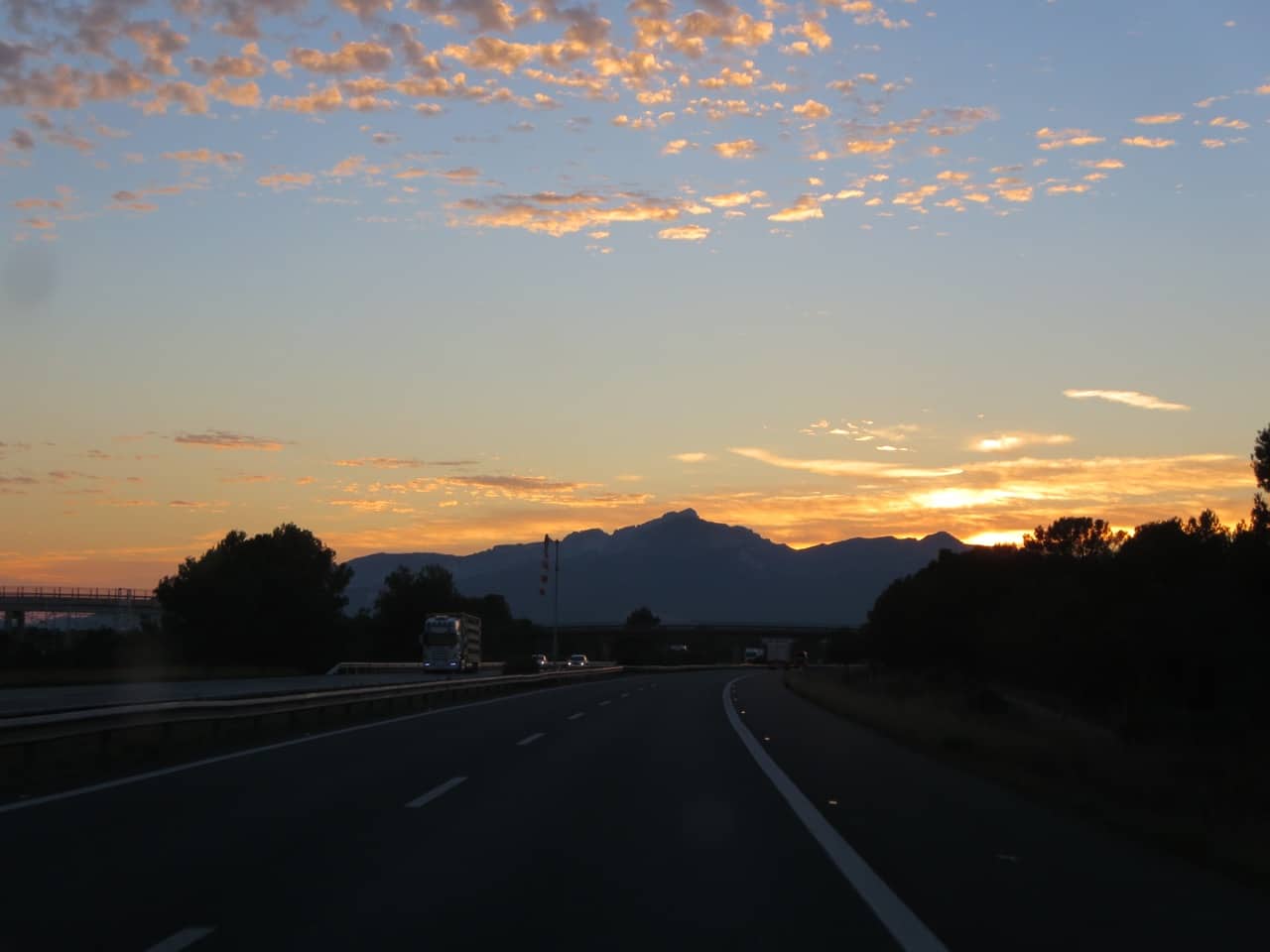 Sonne geht hinter Bergen auf einer Autobahn unter