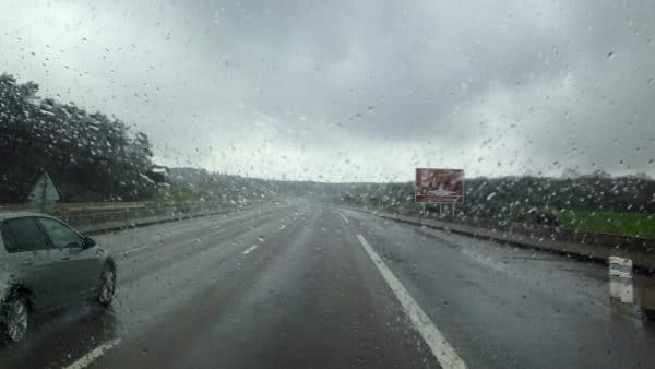 Eine regennasse Autobahn aus einer Scheibe mit Regentropfen heraus fotografiert