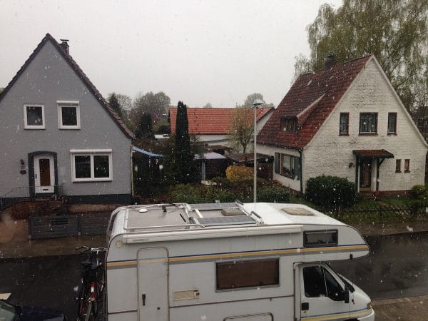 Ein Wohnmobil steht in einer Straße vor zwei Häusern, draußen schneit es