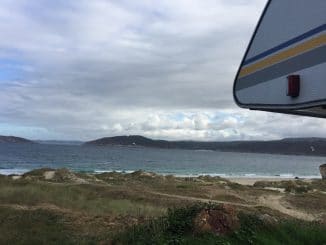 Blick an einem Wohnmobil vorbei auf einen Strand und das Meer mit zwei Kitesurfern
