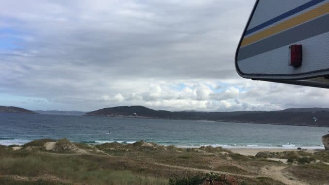 Blick an einem Wohnmobil vorbei auf einen Strand und das Meer mit zwei Kitesurfern