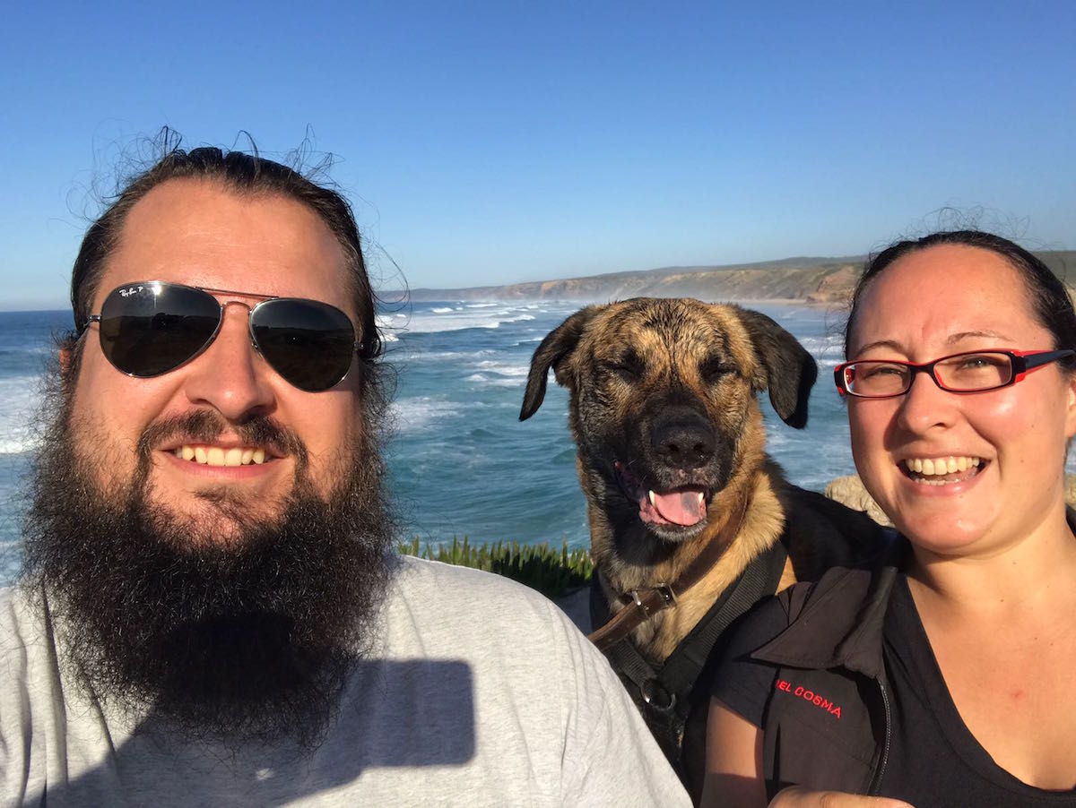 Selfie von einem glücklichen Päarchen in der Mitte ein Hund hinter ihnen das Meer