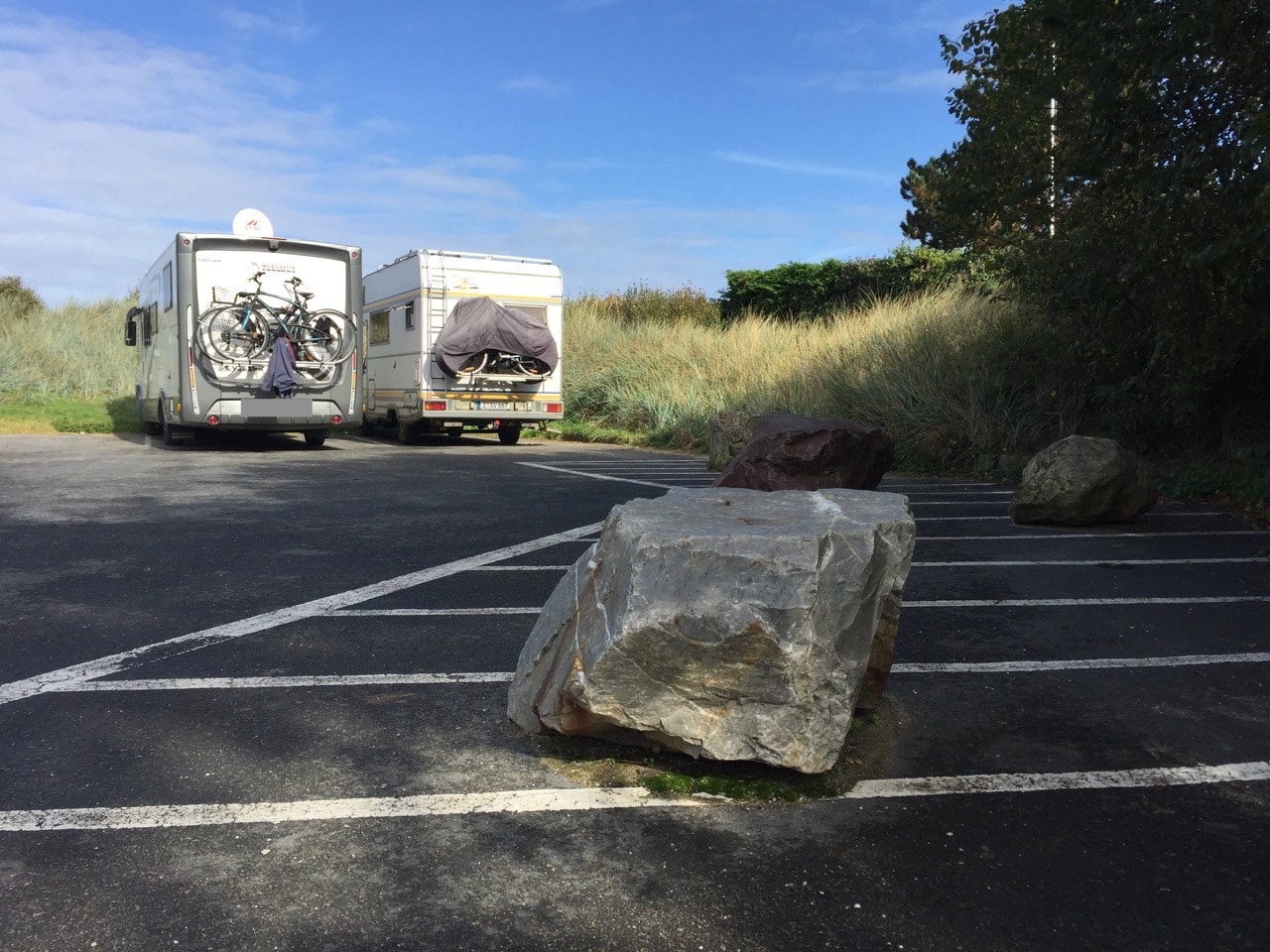 Im Vordergrund ein Stein, im Hintergrund zwei neben einander stehende Wohnmobile vor einer Düne.